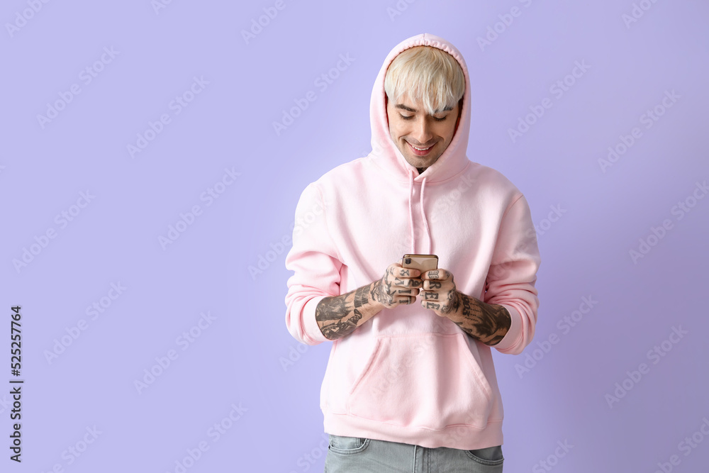 Naklejka premium Young tattooed man in pink hoodie using mobile phone on lilac background