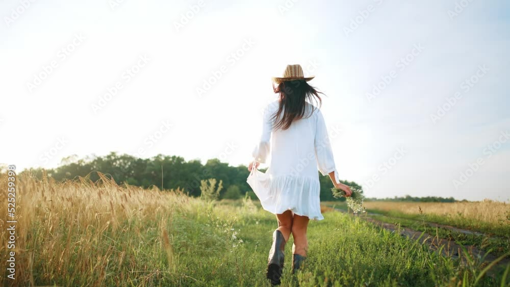 Rear view of young woman running through chamomile field in beautiful summer dress and holding in her hand bouquet of newly collected wild flowers of daisies. Enjoying summer and nature outdoors. Rear view of young woman running through chamomile field in beautiful summer dress and holding in her hand bouquet of newly collected wild flowers of daisies. Enjoying summer and nature outdoors.