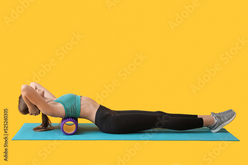 Young woman training with purple foam roller on yellow background photo