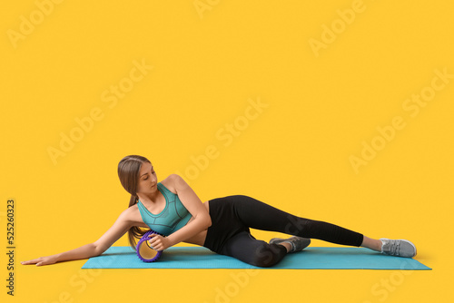 Young woman training with purple foam roller on yellow background photo