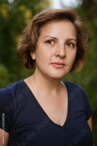 Close-up adult woman portrait against natural jelly background happy and calm smiling during the day in the park in spring or summer