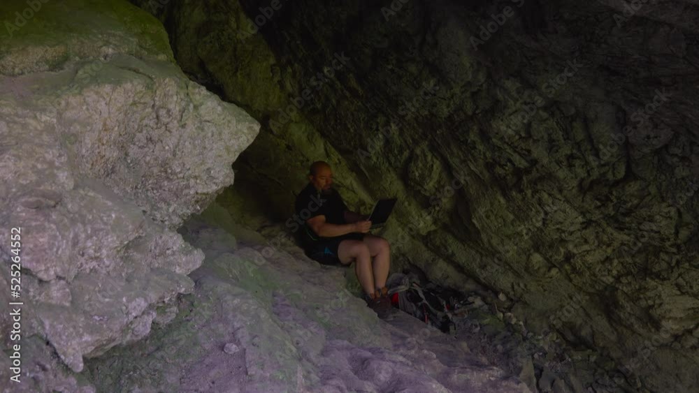 Hiker with laptop working from a cool cave. Concept work from nature in hot summer Hiker with laptop working from a cool cave. Concept work from nature in hot summer