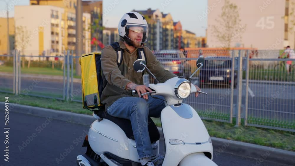 A courier rides a scooter on the road in sunny weather. City delivery service A courier rides a scooter on the road in sunny weather. City delivery service