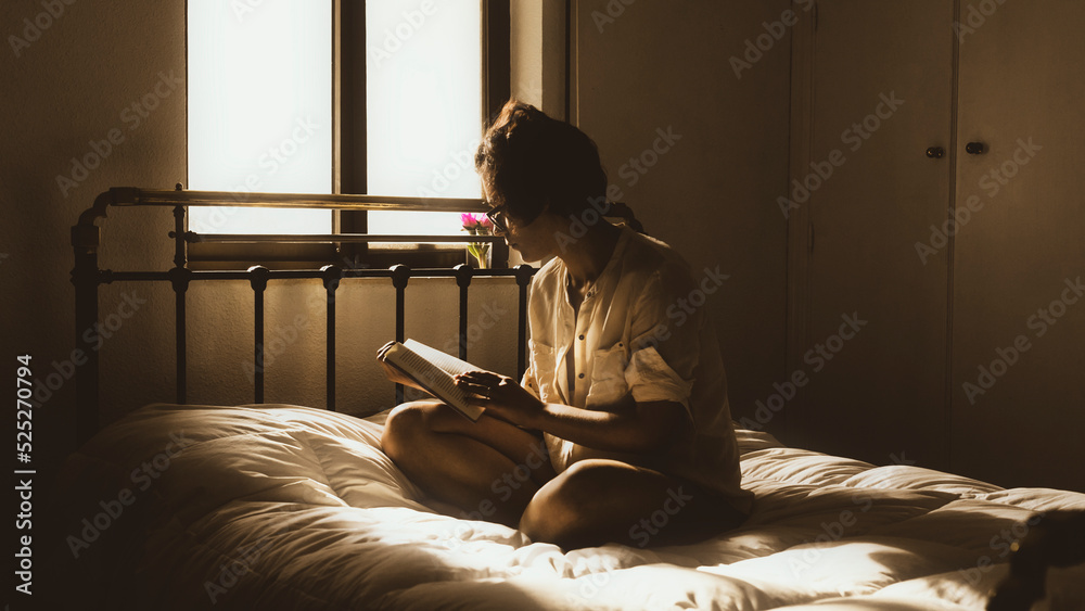 panoramic view of a happy woman in her room at sunset reading a book dressed in a silk shirt. A woman sits near the window and holds a book in her hands. woman reading a book alone. Woman reader panoramic view of a happy woman in her room at sunset reading a book dressed in a silk shirt. A woman sits near the window and holds a book in her hands. woman reading a book alone. Woman reader