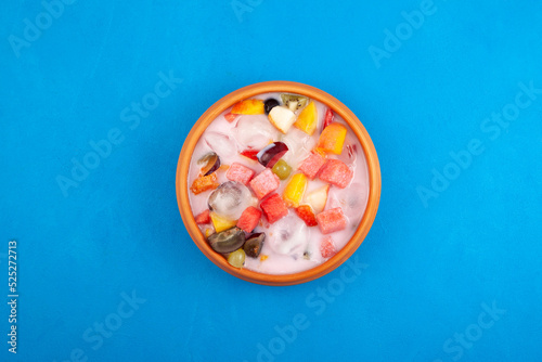 Sop Buah or Es Campur in clay plate on blue background, top view. Mixed fruit cocktail. Es buah Indonesian popular fruit ice with grass jelly, syrup and milk photo
