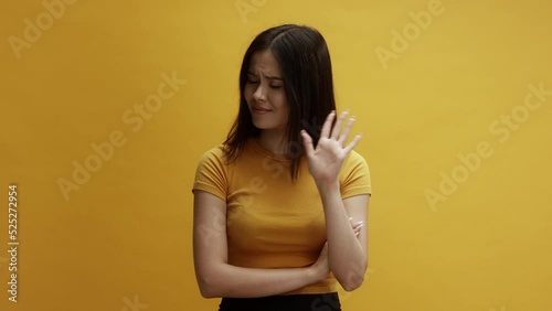 A young asian woman on a yellow background wagging her finger, saying no, disagreeing  photo