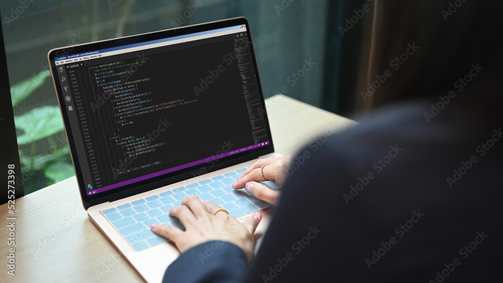 Over shoulder view of female software developer working on web site project, programming on desktop computer in startup company Over shoulder view of female software developer working on web site project, programming on desktop computer in startup company