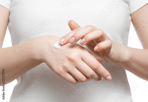 Cropped shot of a woman in white t-shirt applying hand cream  isolated on white. Well-groomed short natural nails.