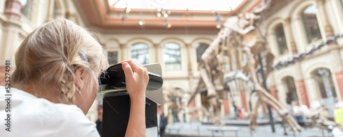 Photography Cute little adorable curious blond kid girl watching AR reality binoculars exploring dinosaur skeleton exposition at german nature history museum