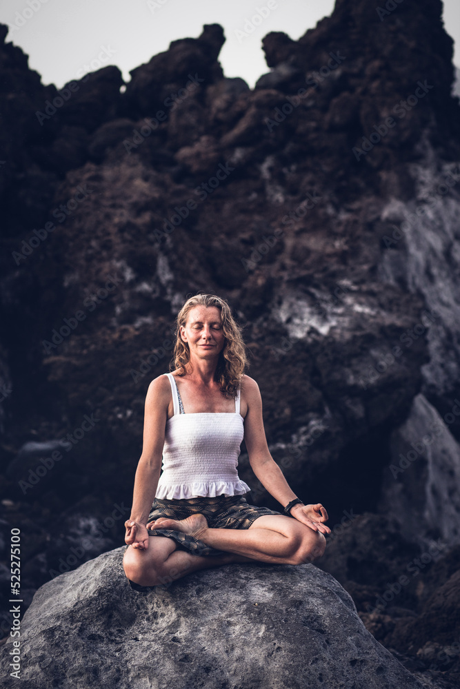 beautiful woman sitting in meditation against dark rocks