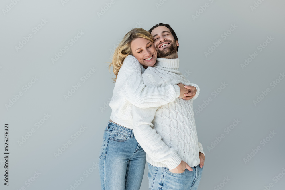 cheerful woman hugging man in white sweater posing with hands in pockets isolated on grey cheerful woman hugging man in white sweater posing with hands in pockets isolated on grey