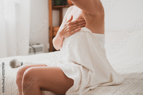 Young woman examines her breasts and lymph nodes with her hands while sitting at home in the bedroom