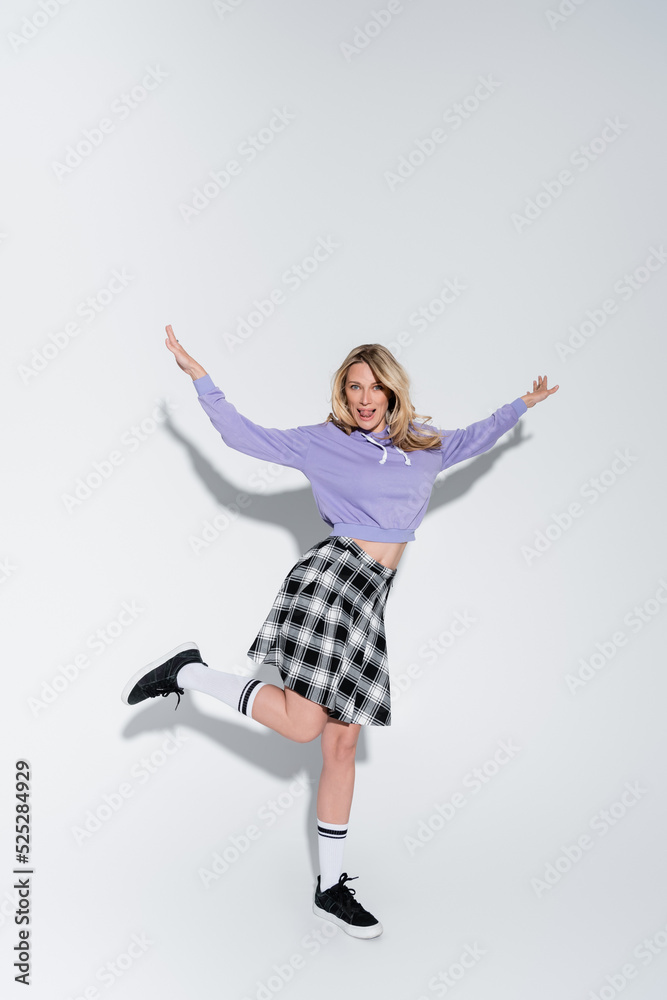 full length of cheerful blonde woman in trendy outfit posing with outstretched hands on grey full length of cheerful blonde woman in trendy outfit posing with outstretched hands on grey