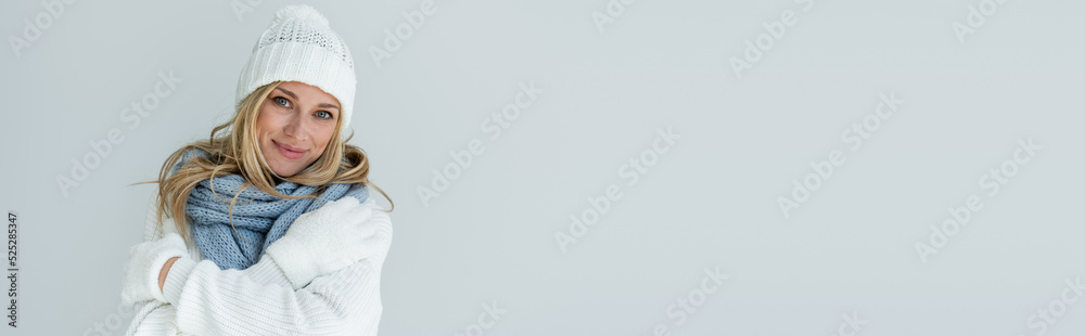 portrait of happy woman in winter hat and knitted scarf looking at camera isolated on grey, banner portrait of happy woman in winter hat and knitted scarf looking at camera isolated on grey, banner
