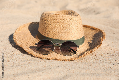 Stylish straw hat and sunglasses on sandy beach