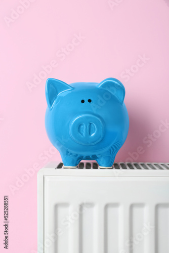 Piggy bank on heating radiator against pink background