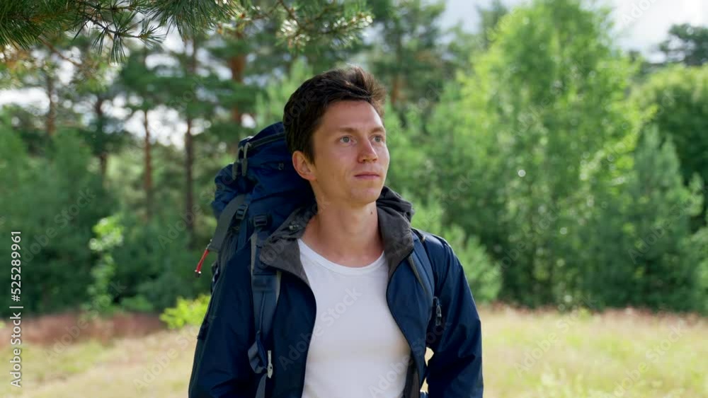 Black-haired guy hiker with blue backpack enjoys walking in forest. Young man discovers awesome landscape hiking in forest with smile on sunny day Black-haired guy hiker with blue backpack enjoys walking in forest. Young man discovers awesome landscape hiking in forest with smile on sunny day