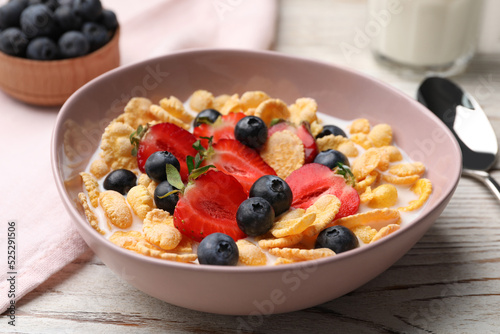 Bowl of tasty crispy corn flakes with milk and berries on white wooden table, closeup