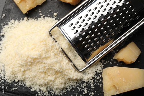 Pile of grated parmesan cheese and grater on black table, flat lay photo