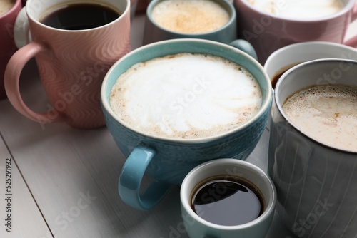 Many different cups with aromatic hot coffee on white wooden table