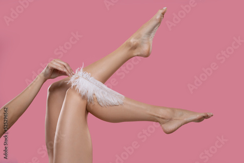 Young Woman's Hand Touhing Her Legs With White Feather On Pink Background. Body Care Concepts. photo