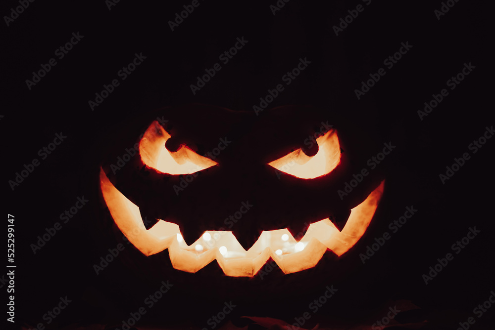 Naklejka premium Spooky smile and sinister eyes of the pumpkin in the darkness. Illuminated face of jack-o-lantern isolated on black background