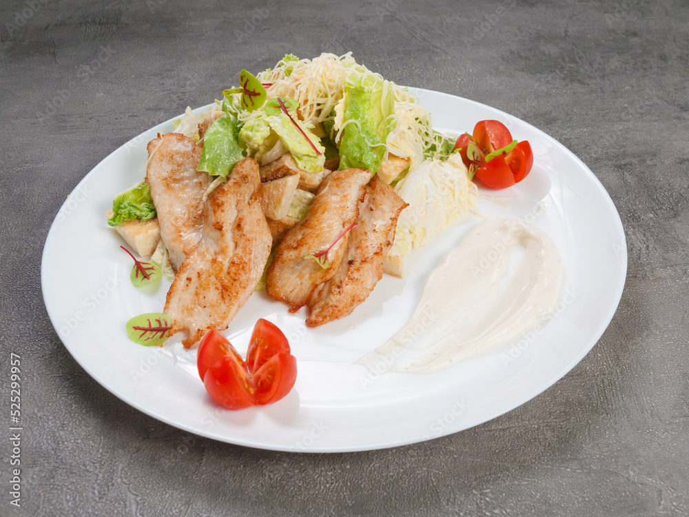 caesar salad with chicken on a white plate on a gray background