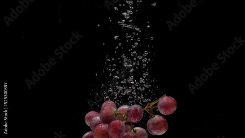 Slow motion red grapes falling into transparent water on black background. Fresh fruit splashing in aquarium. Healthy food, diet, air bubbles