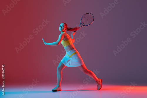 Full length portrait of young woman playing tennis isolated on dark background in neon. Healthy lifestyle, fitness, sport, exercise concept. © master1305