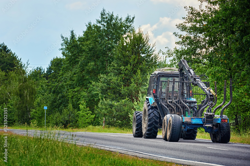 Tractor with empty log trailer with hydraulic grapple moving on contry road. Tractor with trailer for logging. Log carrier machine. Tree harvester vehicle, forestry tractor for harvesting wood.