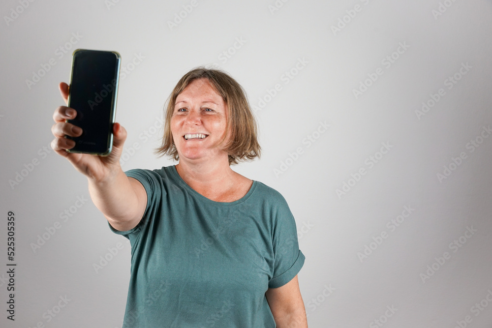 Naklejka premium Eine Frau über 50 macht ein Selfie mit einem Smartphone. Studio, neutraler Hintergrund.