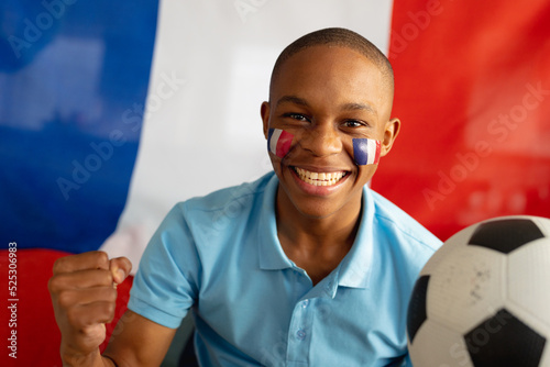 Portrait of happy african american male teenager sitting with flag of france and football