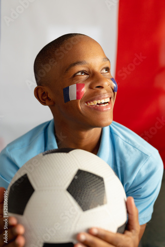 Happy african american male teenager sitting with flag of france and football