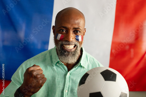 Portrait of happy senior african american man sitting with flag of france and football