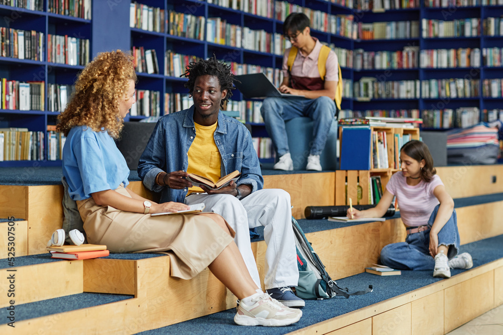 © Seventyfour - Diverse group of college students in library lounge, focus on black young man talking to friend