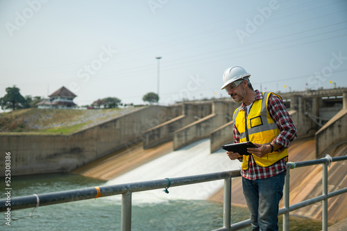 Portrait of engineer wearing yellow vest and white helmet with tablet Working day on a water dam with a hydroelectric power plant. Renewable energy systems, Sustainable energy concept