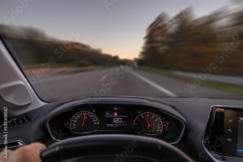 Driver view to the speedometer at 120 kmh or 120 mph and the road blurred in motion, night fall view from inside a car of driver POV of the road landscape.