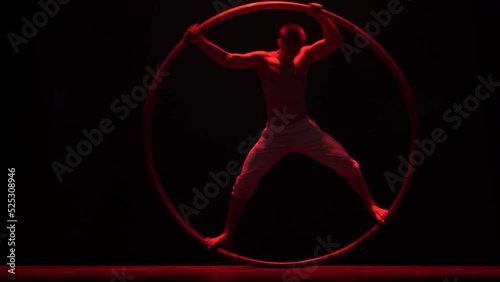 Muscular circus artist perform Cyr Wheel on a black background stage. Concept of motion and movement