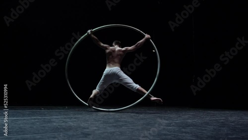 Muscular circus artist perform Cyr Wheel on a black background. Concept of Individuality and creativity 