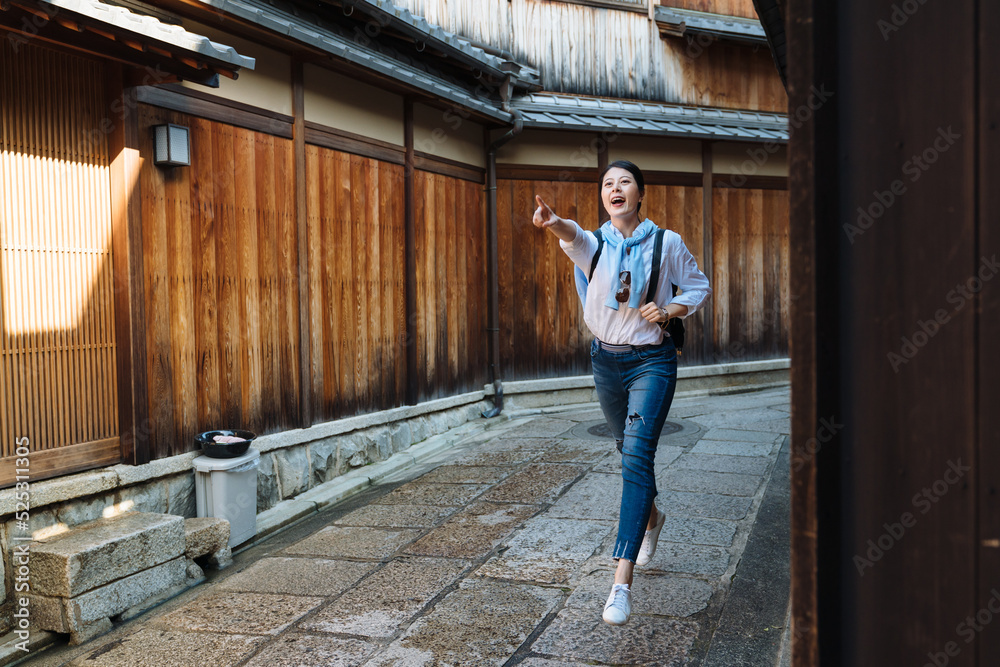full length excited asian female tourist is shouting and pointing into distance while running forward the famous sight she spotted at Ishibe Alley gion, japan
