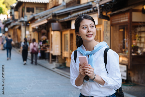 cheerful asian female backpacker is smiling and looking into the distance with a mobile phone in hands while enjoying visiting sannen zaka street in Kyoto japan photo