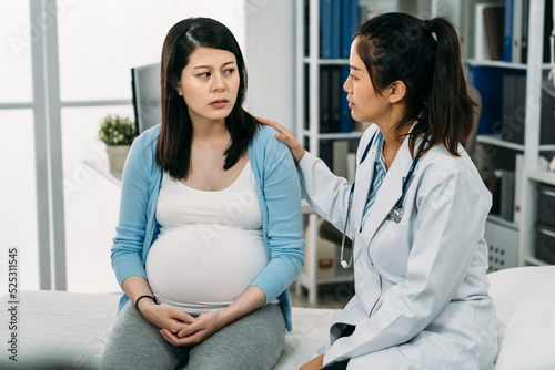 asian pregnant woman suffering depression is looking at her psychologist doctor who is patting on her shoulder showing support during consultation in the clinic