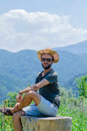 Male model sitting on stump tree. Handsome male portrait. Natural landscape. mountains and woodland in the background 