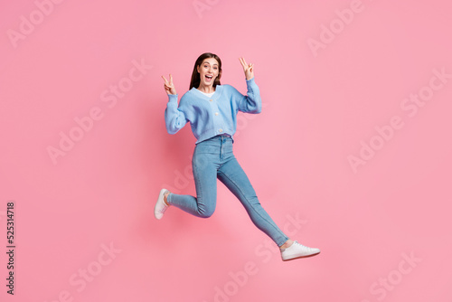 Full size length photo of cute nice toothy girl open mouth jumping in air showing v-sign isolated on pink color background