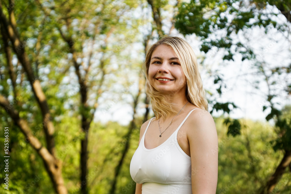 Beautiful young blonde in the forest. The girl enjoys nature on a summer sunny day against the background of green trees. Close portrait Beautiful young blonde in the forest. The girl enjoys nature on a summer sunny day against the background of green trees. Close portrait