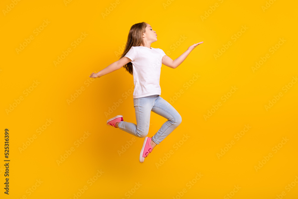 Full length photo of cute flirty school girl wear white t-shirt jumping high sending kiss empty space isolated yellow color background