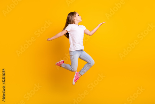 Full length photo of cute flirty school girl wear white t-shirt jumping high sending kiss empty space isolated yellow color background