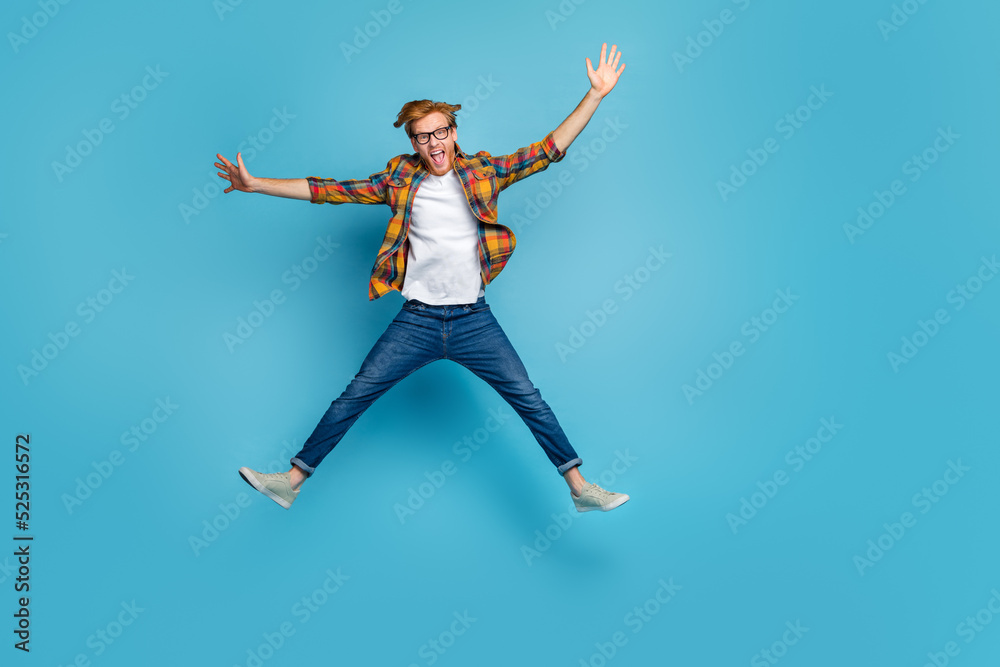 Photo of funky handsome good mood guy open mouth dressed plaid shirt jumping impressed hands to side isolated on blue color background