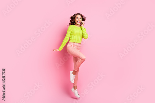 Full body photo of brunette funky lady jump tell telephone wear green shirt pants sneakers isolated on pink color background