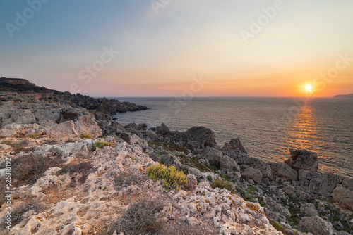 A colourful sunset over the cliffs of Paradis bay in Malta with a view on the Island of Gozo in the Mediterranean Sea. In summer the countries around the Mediterranean enjoy every evening these sunset